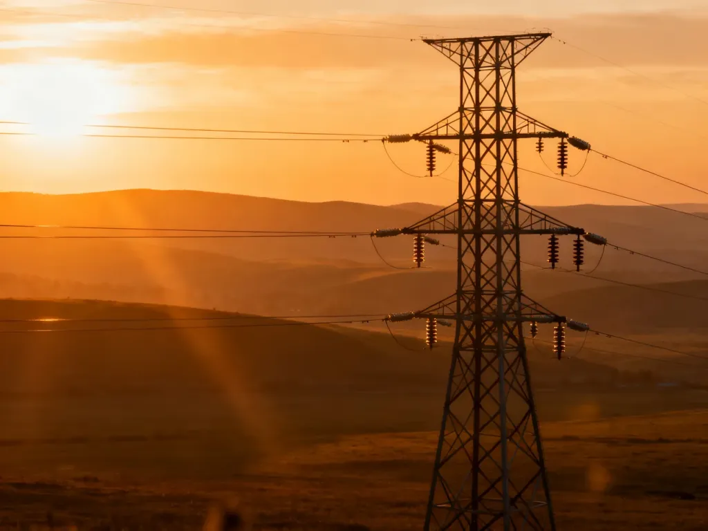 Wysokonapięciowy słup energetyczny na tle zachodzącego słońca, ilustrujący infrastrukturę przesyłową energii elektrycznej.